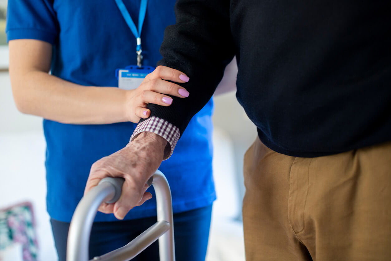 Senior Man With Hands On Walking Frame With Care Worker During Home Health Services.